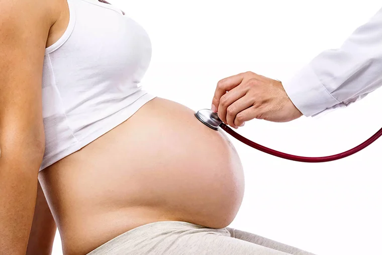 доктор слушает живот беременной женщины перед родами